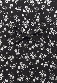 Tissu noir avec un motif floral blanc ; présente un petit détail en forme de nœud. La texture semble lisse avec une légère finition côtelée.