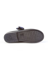 Suela de zapato negro de niño con textura antideslizante y número de talla 25, mostrando el patrón de la suela y la parte superior parcial con un lazo azul.