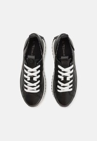 Paire de baskets noires avec lacets blancs et semelles blanches, vues de dessus sur un fond clair, taille 37 indiquée à l'intérieur des chaussures.