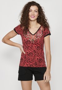 T-shirt floral rouge avec bord noir et col en V, présentant une broderie florale détaillée sur la poitrine. Associé à un short noir.