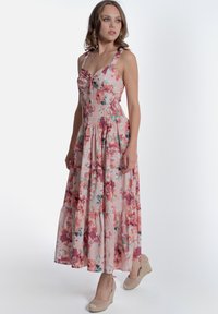 Abito maxi floreale rosa, con un corpetto aderente e dettagli arricciati, spalline larghe e una gonna a più strati. Indossato con sandali con zeppa beige.