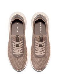 Hnědé pletené tenisky s texturovaným svrškem, elastickými tkaničkami a světlou podešví. Jsou vybaveny značkovými vložkami a hladkými špičkami.