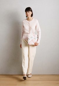 Cardigan rose clair avec des boutons, pantalon large crème, et un sac à motifs floraux. Textures douces avec des accents subtils.