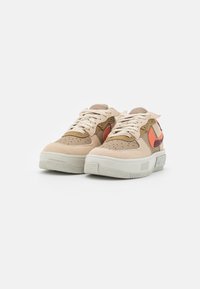 Beige mockasneakers med orange och bruna detaljer, perforerad design, platta snören och texturerad gummisula.