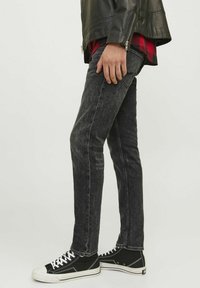 Jean de denim negro ajustado con un ligero desvanecimiento, diseño clásico de cinco bolsillos, combinado con zapatillas negras de caña alta y una chaqueta de cuero.