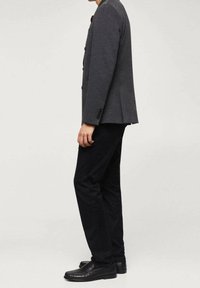 Blazer grigio con vestibilità sartoriale, caratterizzato da una fila singola di bottoni, abbinato a pantaloni neri e scarpe in pelle nera. Texture liscia, design minimalista.