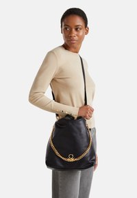 Borsa a spalla in pelle nera con cintura in catena dorata, caratterizzata da un design morbido e sformato e un distintivo dettaglio in metallo circolare.