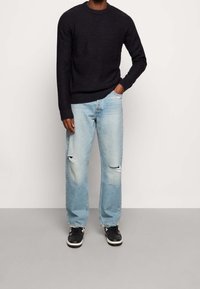 Stickad mörk tröja med rund hals, parat med ljusblå slitna jeans med revor. Bärs med svart och vita sneakers.