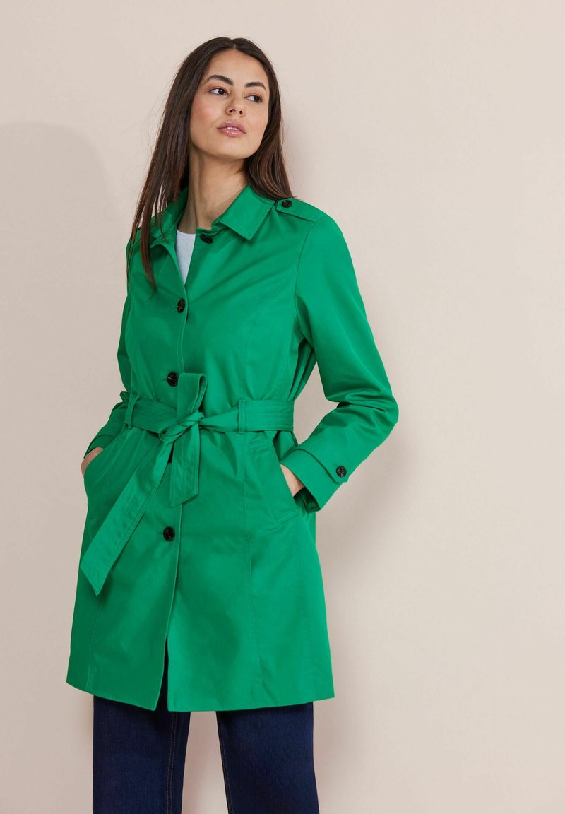 Grön trenchcoat med bälte i midjan, med spetsig krage och knappstängningar. Tillverkad av ett smidigt, lätt material.