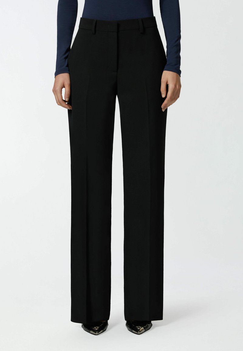 Crne krojene hlače s visokim strukom, ravnim nogavicama i bočnim nabora. Glatka tkanina s finom teksturom. Vidljive su crne cipele s oštrim vrhom.