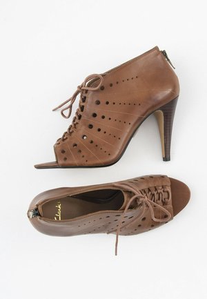 Brune læder ankelstøvler med høje hæle, åben tå-design, snørrebånd foran, perforerede detaljer og lynlås lukning i siden.