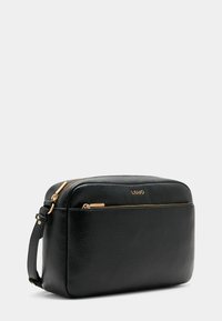 Sac en cuir noir avec une finition texturée, quincaillerie en ton doré, fermeture éclair et une seule sangle réglable. Logo de la marque sur le devant.