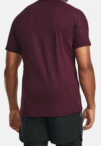 Camiseta deportiva burdeos con mangas cortas, tela texturizada y detalles de costura. La vista desde atrás muestra un diseño liso y ajustado.