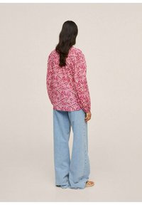 Camisa de manga larga con estampado floral en rosa, combinada con pantalones vaqueros de pierna ancha en azul claro. La camisa tiene un corte relajado y una textura especial.