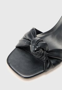 Černá kožená sandal s čtveratou špičkou a uzlovým detailem vpředu. Hladký povrch a minimalistický design. Neutrální podrážka.
