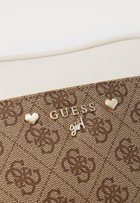 Borsa a mano marrone con motivo, realizzata in tessuto testurizzato, con accessori in metallo dorato e rifinitura in pelle bianca. Accenti decorativi a forma di cuore e dettaglio del logo.