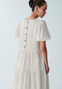 Kermapunainen mekko, jossa on pystysuorat beige-raitakuviot, lyhyet puffihihat ja kerroksellinen muotoilu. Selkäpuolella on napit ja kangas on tekstuuri.