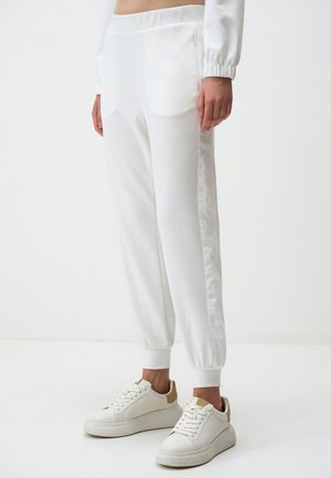 Witte joggerbroeken met elastische boorden en zijritsen, gedragen met witte sneakers met beige accenten.