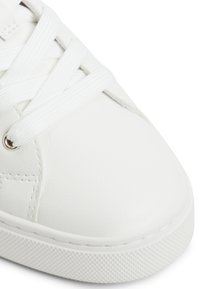 Weiße Sneaker aus glattem, synthetischem Material, mit flachen weißen Schnürsenkeln, einer runden Zehenpartie und einer strukturierten Gummisohle.