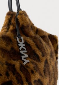 Braune Kunstfelltasche mit einem Leopardenmuster, ausgestattet mit schwarzen Ledergriffen und metallischen Beschlägen, die den Markennamen tragen.
