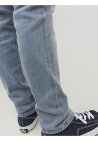 Světle modré džíny s úzkým střihem, s jemným vyblednutím. V kombinaci s tmavě modrými teniskami s bílými šňůrami a silnou bílou podrážkou.