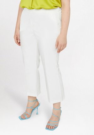 Pantalones recortados blancos con bolsillos laterales y una textura suave. Combinados con sandalias de tacón alto azul con tiras que muestran los dedos de los pies.