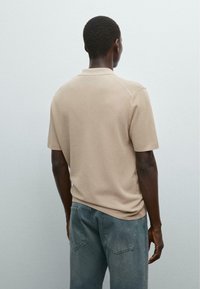 Beige polo shirt met korte mouwen van een gestructureerde brei, met een kraag en een relaxte pasvorm, gecombineerd met lichtblauwe spijkerbroek.