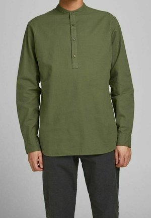 Homme portant une chemise manches longues vert olive avec un col mao et une patte de boutonnage à trois boutons, associée à un pantalon gris foncé.