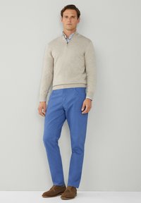Bežna zip-up majica, plave hlače, smeđe cipele. Majica ima teksturiranu završnicu, hlače su glatke s bočnim džepovima, a cipele imaju vezice.
