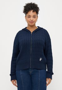 Ναυτικό μπλε φούτερ με φερμουάρ που διαθέτει υφασμάτινο σχέδιο με πλέκτους, ριμπ μανσέτες και στρίφωμα, καθώς και ένα μικρό κεντημένο λογότυπο στο στήθος.