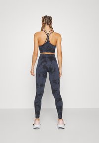 Top court de sport bleu marine avec des bretelles croisées et un legging taille haute assorti présentant un motif tie-dye, associé à des baskets roses.