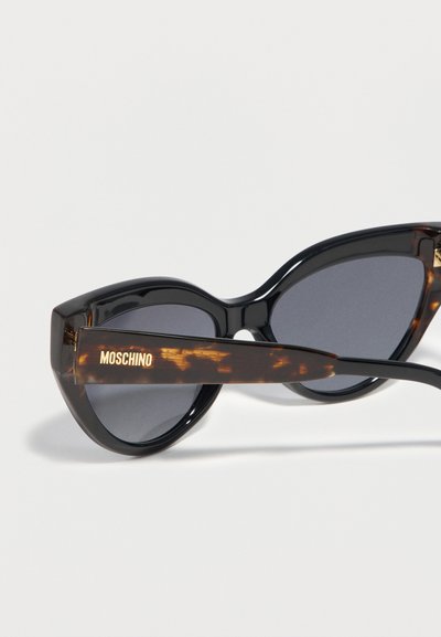 Μαύρα γυαλιά ηλίου τύπου cat-eye με σκούρους φακούς και βραχίονες από σχέδιο χελώνας, με χρυσή επωνυμία Moschino.