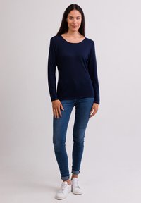 Maglietta a maniche lunghe blu navy con scollo rotondo, abbinata a jeans blu aderenti e sneaker bianche, creando un outfit casual.