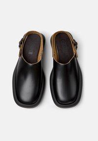 Zoccoli di pelle nera con punta quadrata, apertura sul retro e dettagli color cammello. Presentano una cinturino con fibbia e una soletta testurizzata per il comfort.
