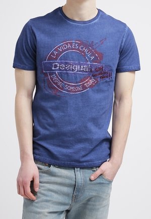 Niebieska koszulka graficzna z bawełny, krótki rękaw, z okrągłym nadrukiem z tekstem w wielu kolorach i postarzanymi detalami.