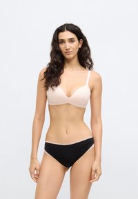 Gaiši rozā krūšturis ar dziļu izgriezumu un plānām lencēm, kopā ar melniem bikini biksītēm ar bēša krāsas apmali vidukļa joslā.