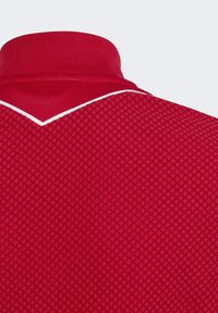 Rotes Poloshirt mit strukturiertem Muster, spitzem Kragen und weißen Einsätzen entlang des Kragenrandes.