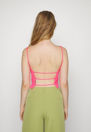 Top aderente di un brillante rosa, con spalline sottili e schiena scoperta, caratterizzato da fasce orizzontali. Abbinato a pantaloni verdi a vita alta.