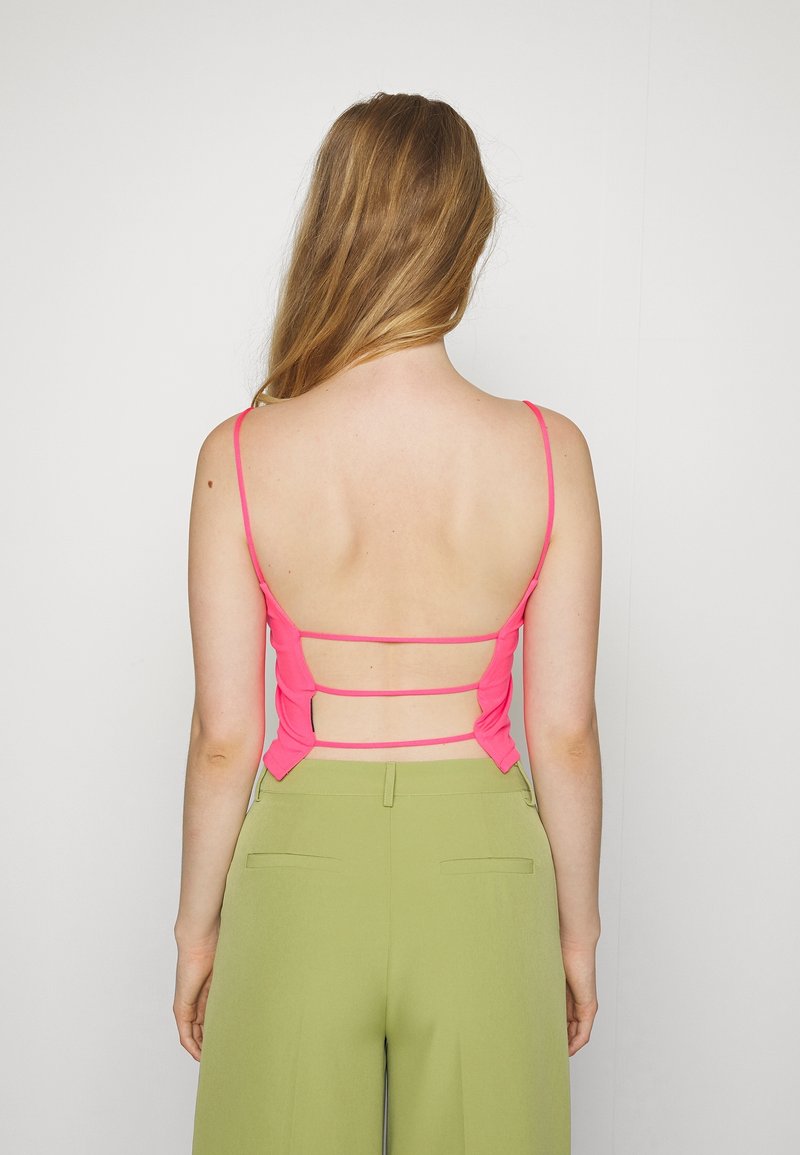 Upnutý jasně růžový top s tenkými ramínky, který má otevřený design zad a horizontální pásky. Kombinováno s kalhotami s vysokým pasem v zelené barvě.