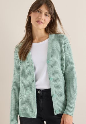 Mintgroene gebreide cardigan met een knoopsluiting aan de voorkant, geribbelde textuur en een ronde halslijn over een witte top. Zwarte broek en knopen zichtbaar.