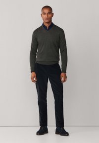 Donkergrijze v-halstrui over donkerblauwe broek, gecombineerd met donkerblauwe schoenen. Soepele texturen; minimale details; getailleerde pasvorm.