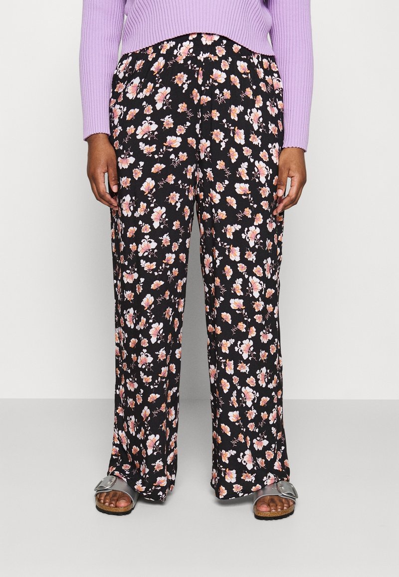 Person wearing black wide-leg pants with pink and white floral print, a lavender ribbed sweater, and silver open-toe sandals.