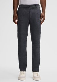 Strukturierte, dunkelgraue Hose mit Schnitt, ausgestattet mit Seitentaschen, vorderem Knopfverschluss und glattem Bund. Getragen mit weißen Sneakers.