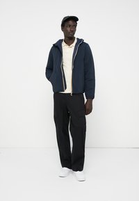 Navy puffer jacket with a zipper and hood, paired with a beige polo shirt and black cargo pants. White sneakers. Plain background.