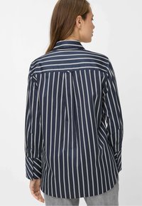 Camicia a righe blu navy con strisce verticali bianche, maniche lunghe, polsini con bottoni e piega posteriore per maggiore libertà di movimento.