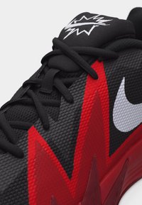 Baskets texturées noires et rouges avec des lacets noirs, le logo Nike swoosh blanc et un éclair sur la languette.