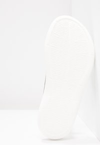Semelle de sneaker blanche avec un motif de traction en caoutchouc texturé, présentant une forme arrondie et une surface lisse et continue le long des bords.