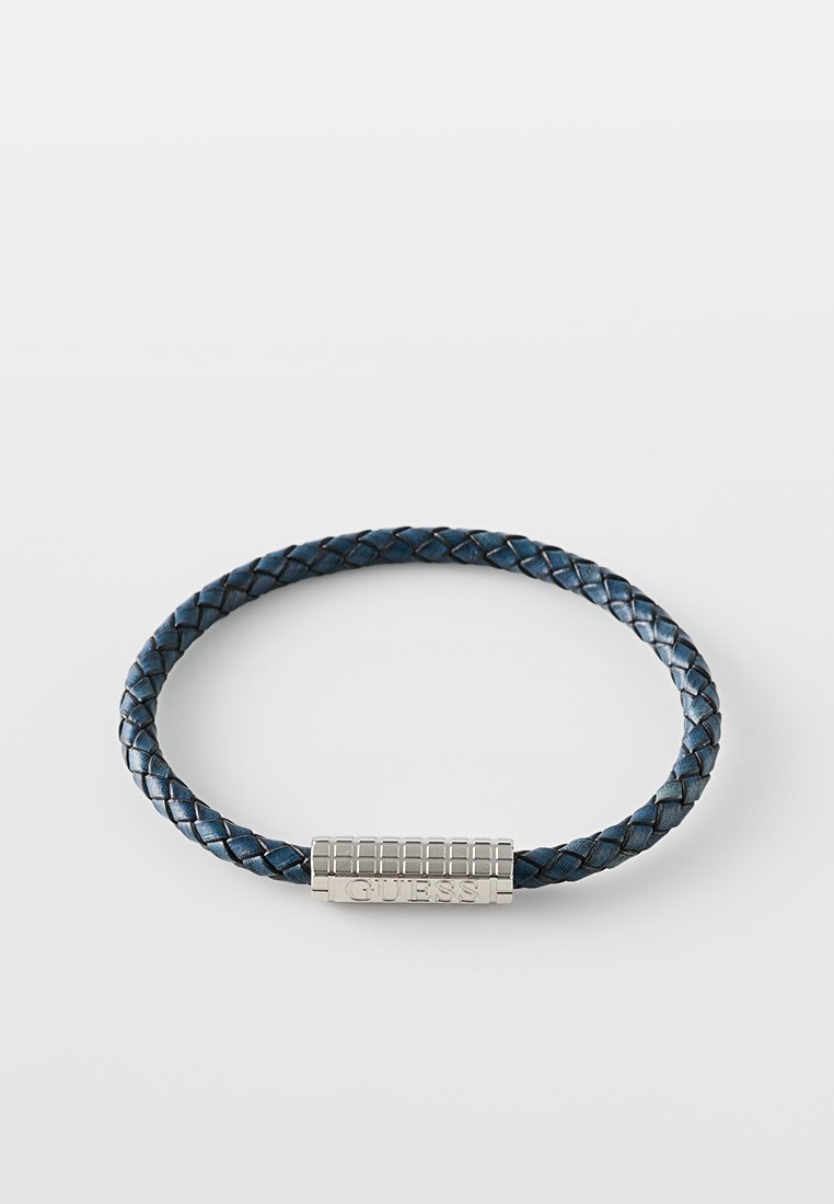 Bracelet en cuir tressé bleu avec fermoir rectangulaire en argent portant le mot gravé "GUESS". Texture lisse et forme arrondie.