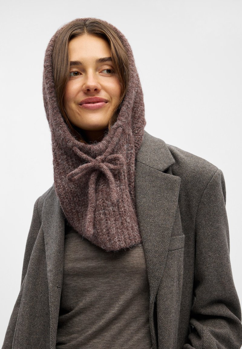 Knitted, brownish-pink hood scarf with a textured pattern and bow accent. Worn over a gray shirt and jacket, highlighting a soft, cozy design.