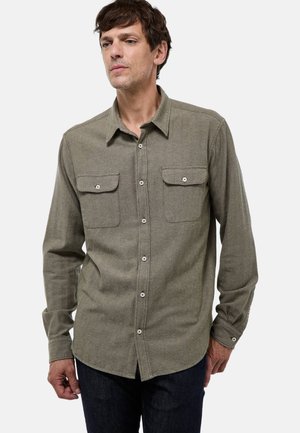 Chemise à manches longues en tissu vert olive, avec un col button-down, deux poches poitrine et des accents de boutons blancs. Texture lisse.